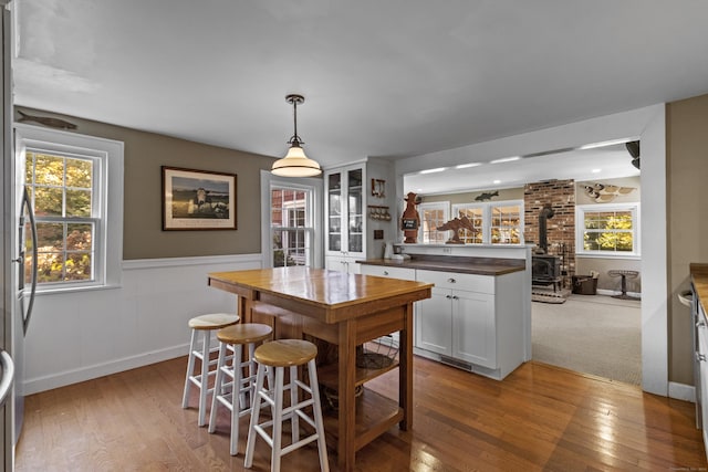 kitchen featuring white cabinets, decorative light fixtures, a wood stove, and light hardwood / wood-style flooring