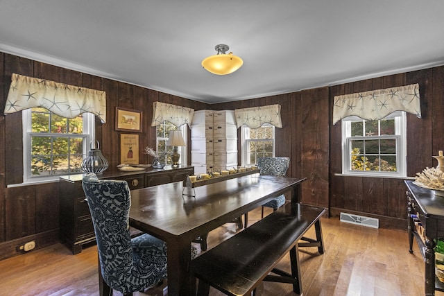 dining room featuring wooden walls, a healthy amount of sunlight, and hardwood / wood-style flooring