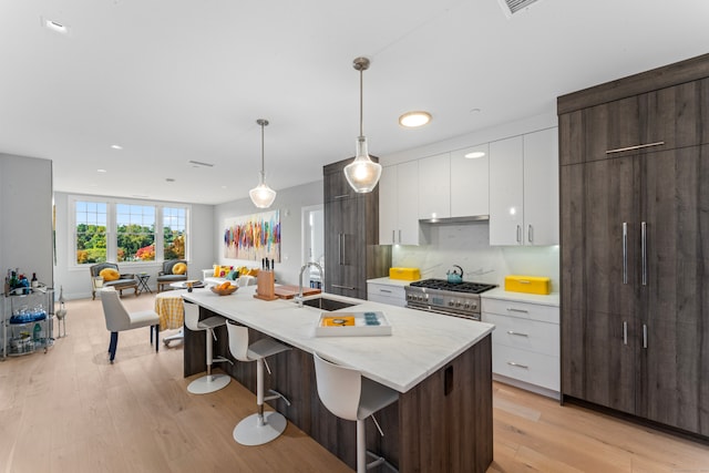 kitchen featuring a kitchen island with sink, hanging light fixtures, sink, dark brown cabinetry, and white cabinets