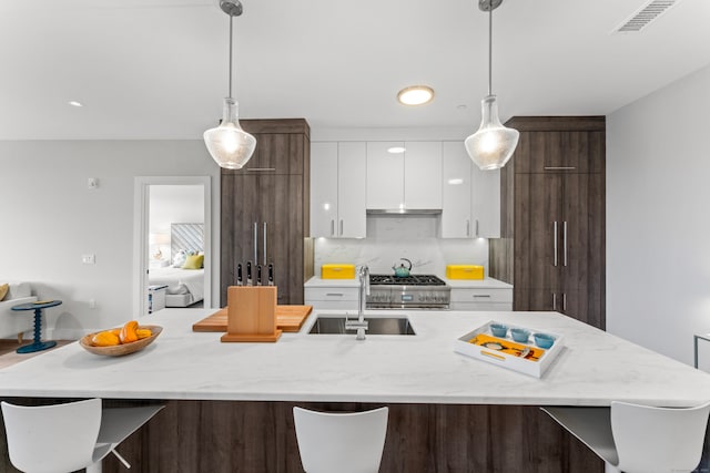 kitchen with sink, an island with sink, dark brown cabinets, white cabinetry, and decorative light fixtures