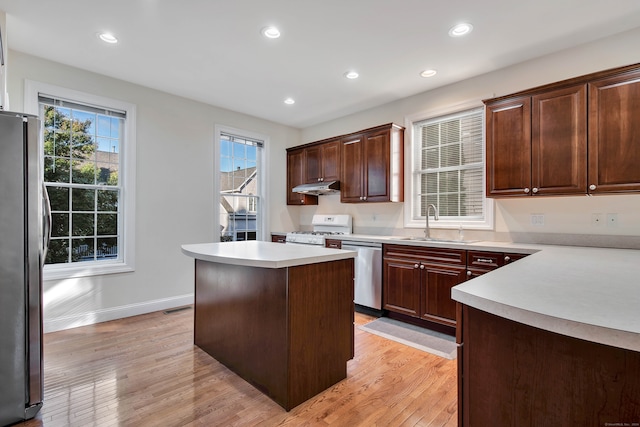 kitchen featuring appliances with stainless steel finishes, sink, a kitchen island, dark brown cabinets, and light hardwood / wood-style flooring