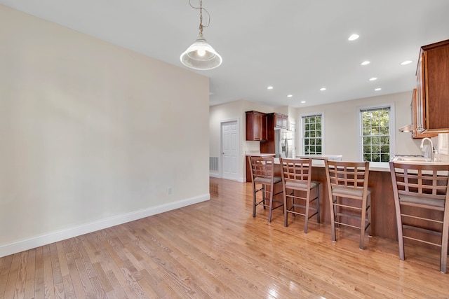 kitchen featuring a kitchen breakfast bar, stainless steel fridge, light hardwood / wood-style flooring, and hanging light fixtures