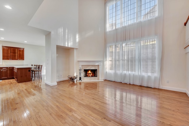 living room with a high end fireplace, a high ceiling, and light hardwood / wood-style floors