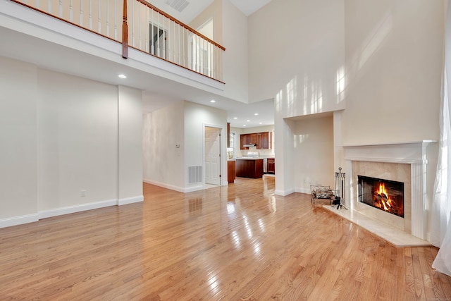 unfurnished living room with a premium fireplace, a high ceiling, and light hardwood / wood-style floors