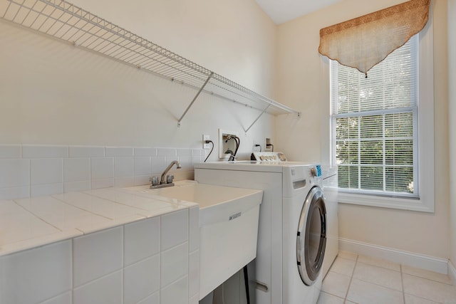 laundry area with sink, light tile patterned flooring, washer and clothes dryer, and plenty of natural light