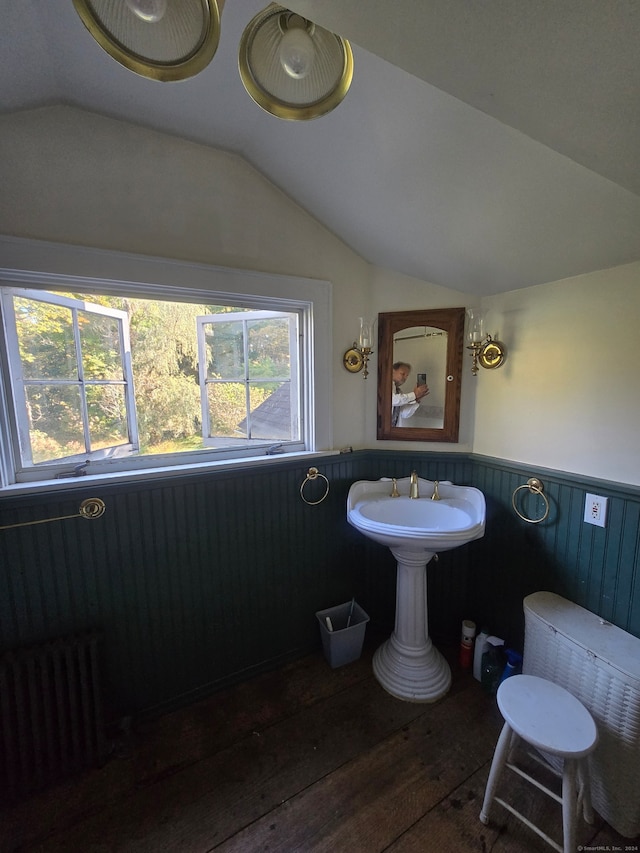 bathroom featuring lofted ceiling, hardwood / wood-style flooring, radiator, wooden walls, and sink