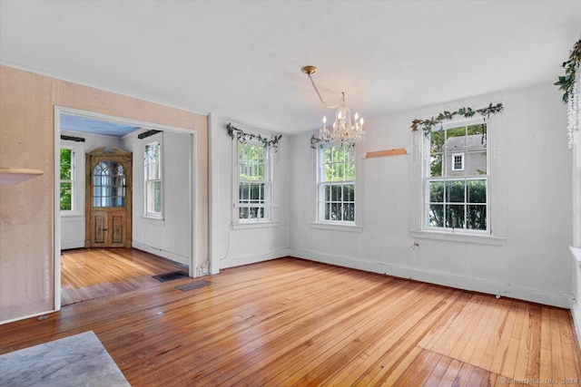 unfurnished room with an inviting chandelier, plenty of natural light, and light wood-type flooring