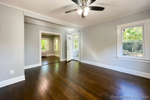 spare room with dark wood-type flooring, ceiling fan, a healthy amount of sunlight, and radiator heating unit