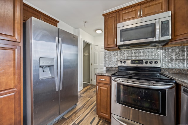 kitchen with appliances with stainless steel finishes, dark stone counters, tasteful backsplash, and light wood-type flooring