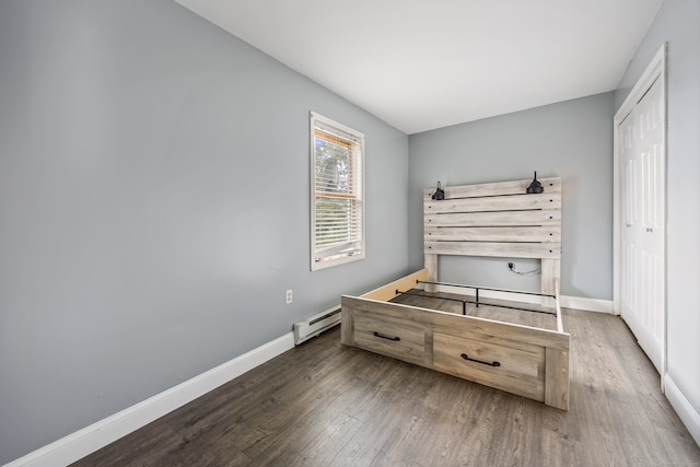 bedroom with dark wood-type flooring, a baseboard heating unit, and a closet