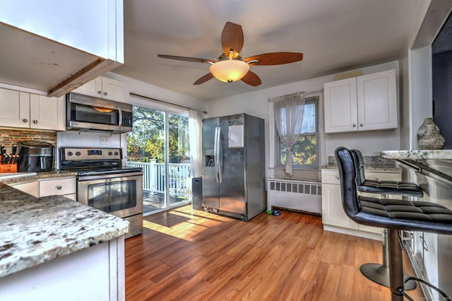 kitchen with appliances with stainless steel finishes, light hardwood / wood-style flooring, white cabinetry, and radiator