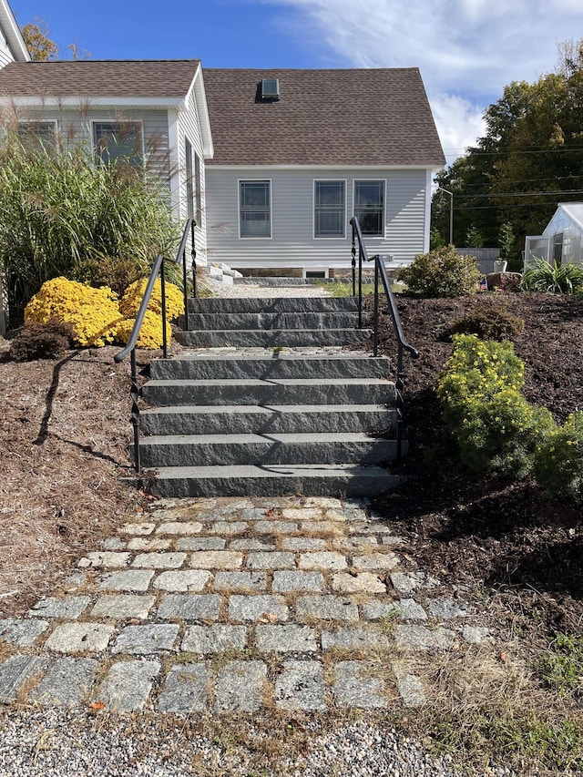 exterior space featuring a shingled roof and stairs