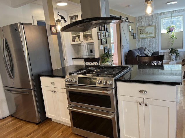 kitchen with island exhaust hood, stainless steel appliances, a barn door, pendant lighting, and white cabinets