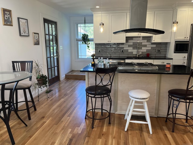 kitchen featuring island exhaust hood, white cabinetry, light wood-type flooring, and a breakfast bar