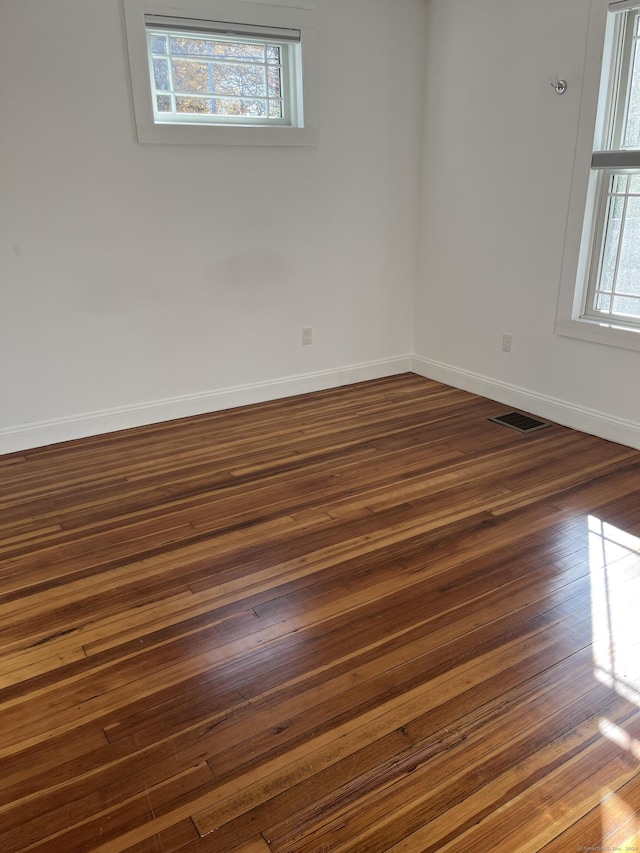unfurnished room with visible vents, baseboards, and dark wood-style flooring