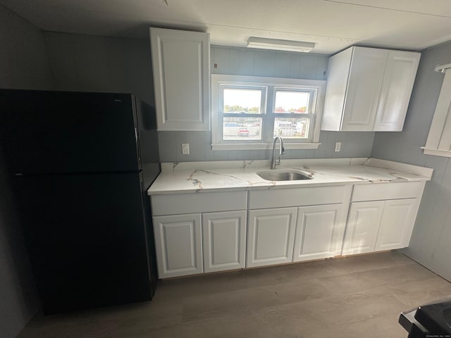 kitchen with light stone countertops, sink, light wood-type flooring, white cabinetry, and black refrigerator