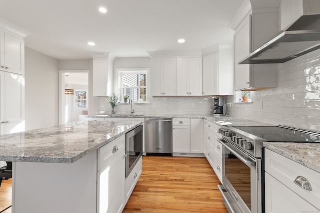 kitchen with light wood-type flooring, stainless steel appliances, wall chimney range hood, white cabinets, and a kitchen island