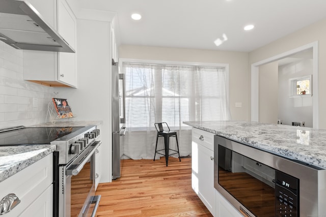 kitchen featuring appliances with stainless steel finishes, light stone counters, wall chimney exhaust hood, light hardwood / wood-style flooring, and white cabinetry