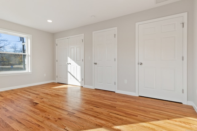 unfurnished bedroom with multiple closets and light hardwood / wood-style floors