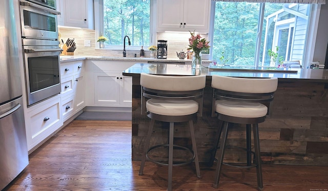 kitchen with appliances with stainless steel finishes, white cabinetry, light stone counters, a kitchen bar, and dark hardwood / wood-style flooring