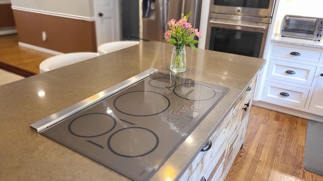 interior details featuring appliances with stainless steel finishes, light stone countertops, light hardwood / wood-style flooring, and white cabinets