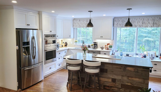 kitchen featuring white cabinetry, a center island, light wood-type flooring, pendant lighting, and stainless steel appliances