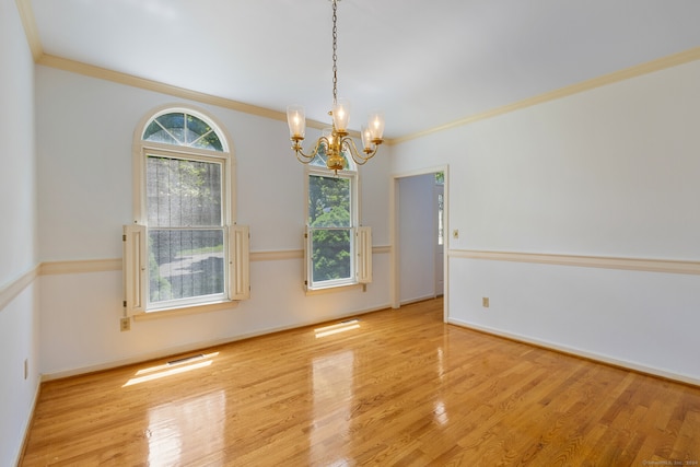 empty room with crown molding, a chandelier, and light wood-type flooring