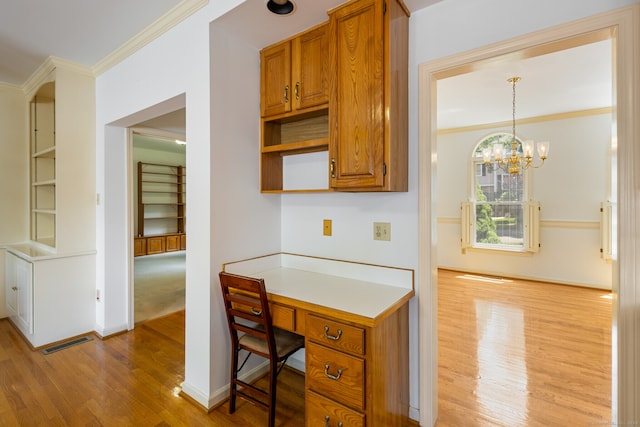 kitchen featuring ornamental molding, decorative light fixtures, light wood-type flooring, and built in desk