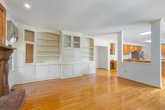 unfurnished living room featuring ornamental molding, light wood-type flooring, and built in shelves