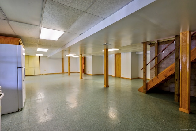 basement featuring a paneled ceiling and white refrigerator