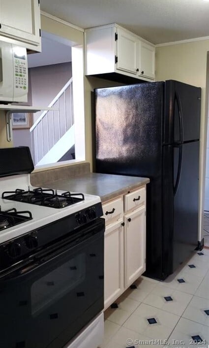 kitchen with white appliances, white cabinetry, light tile patterned flooring, and ornamental molding