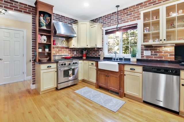 kitchen with wall chimney exhaust hood, sink, appliances with stainless steel finishes, and cream cabinetry