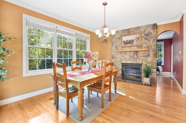 dining space featuring a notable chandelier, crown molding, a stone fireplace, and hardwood / wood-style floors