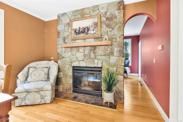 living room with a stone fireplace, crown molding, and hardwood / wood-style floors