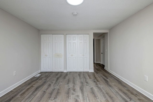 unfurnished bedroom with a textured ceiling, two closets, and wood-type flooring