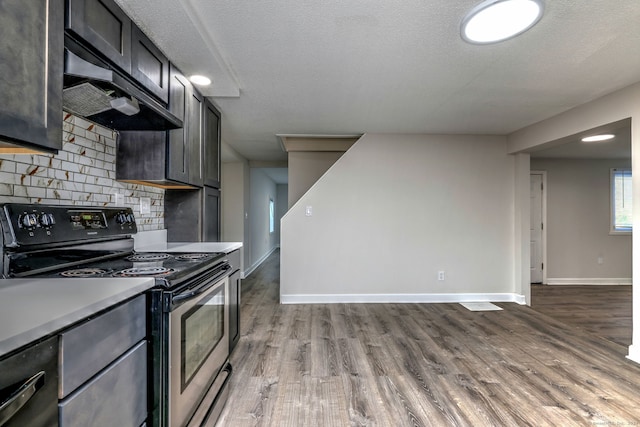 kitchen featuring tasteful backsplash, a textured ceiling, stainless steel electric stove, range hood, and light hardwood / wood-style flooring