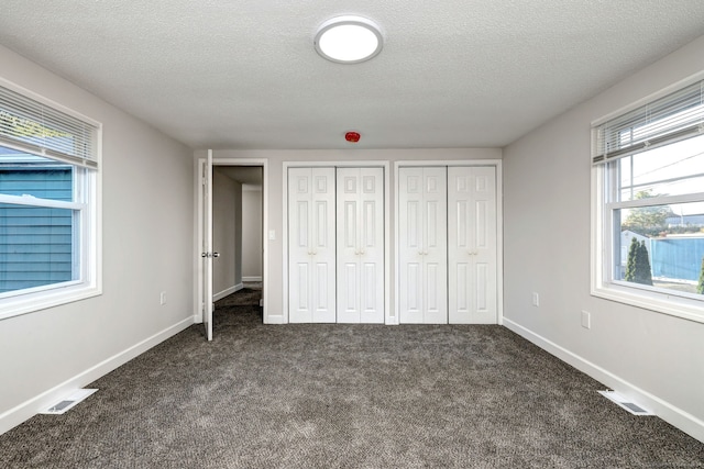 unfurnished bedroom with dark carpet, multiple closets, and a textured ceiling