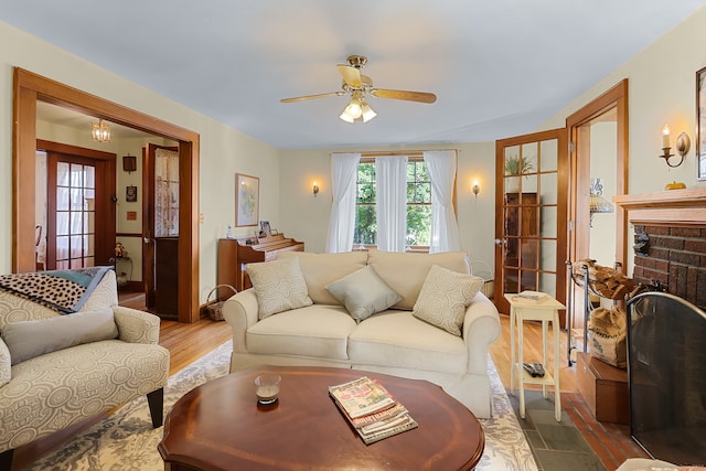 living room with a brick fireplace, wood-type flooring, and ceiling fan