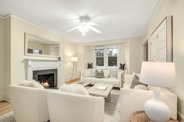 living room with crown molding, a brick fireplace, ceiling fan, and light wood-type flooring