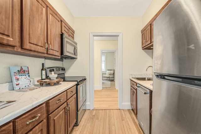 kitchen with sink, light hardwood / wood-style floors, light stone countertops, and appliances with stainless steel finishes