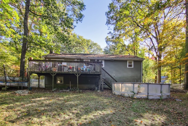 back of house with a trampoline, a swimming pool side deck, and a lawn