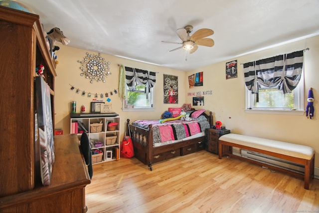 bedroom with ceiling fan, multiple windows, baseboard heating, and light hardwood / wood-style floors