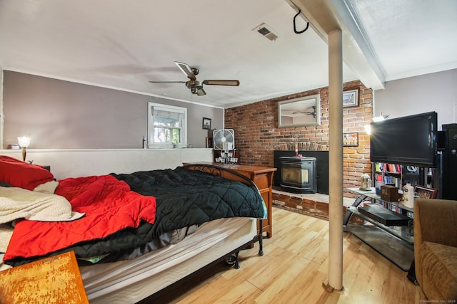 bedroom featuring beamed ceiling, wood-type flooring, a wood stove, crown molding, and ceiling fan