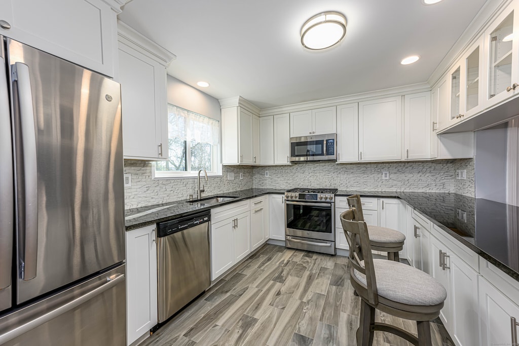 kitchen featuring appliances with stainless steel finishes, sink, light hardwood / wood-style flooring, dark stone countertops, and white cabinets