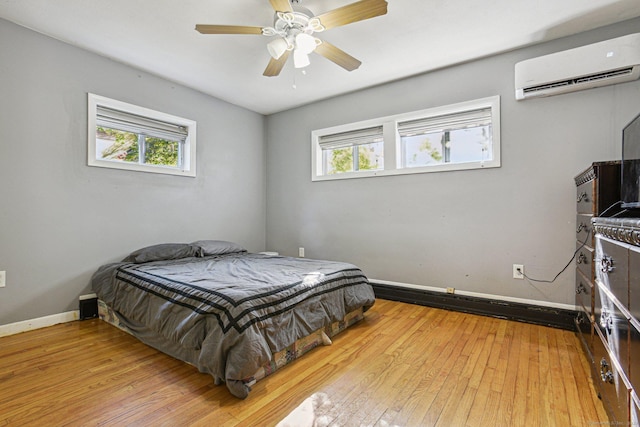 bedroom featuring an AC wall unit, multiple windows, ceiling fan, and light hardwood / wood-style flooring