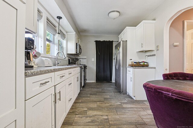 kitchen with pendant lighting, white cabinets, dark hardwood / wood-style floors, appliances with stainless steel finishes, and light stone counters