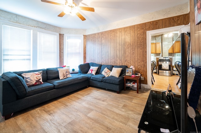 living room with ceiling fan, light wood-type flooring, and wood walls