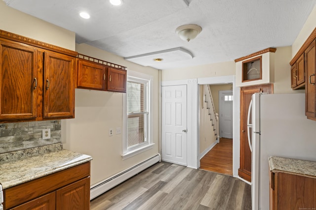 kitchen featuring light stone countertops, a baseboard heating unit, white fridge, wood-type flooring, and decorative backsplash