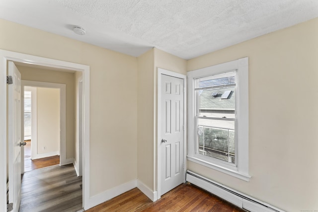 interior space with a textured ceiling, dark hardwood / wood-style floors, and a baseboard heating unit