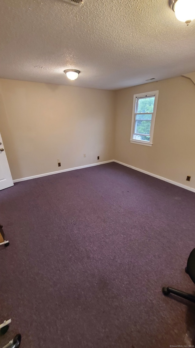 unfurnished room featuring a textured ceiling and dark carpet